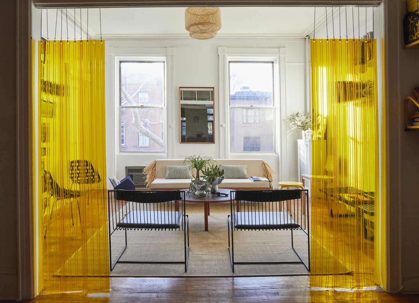 To divide the rooms, Valentin came up with an unconventional solution: yellow strip curtains, the kind typically used in industrial food storage facilities, suspended from a hospital drop chain sourced from a medical supply website. The black metal and leather chairs are Arnold Lounge Chairs from Valentin’s company, Bogus Studio ($980 each); the jute Osted Rug is from Ikea. The light fixture is a rental hack—Ikea’s Sinnerlig Bamboo Shade—to cover up the landlord’s less appealing ceiling fixture.