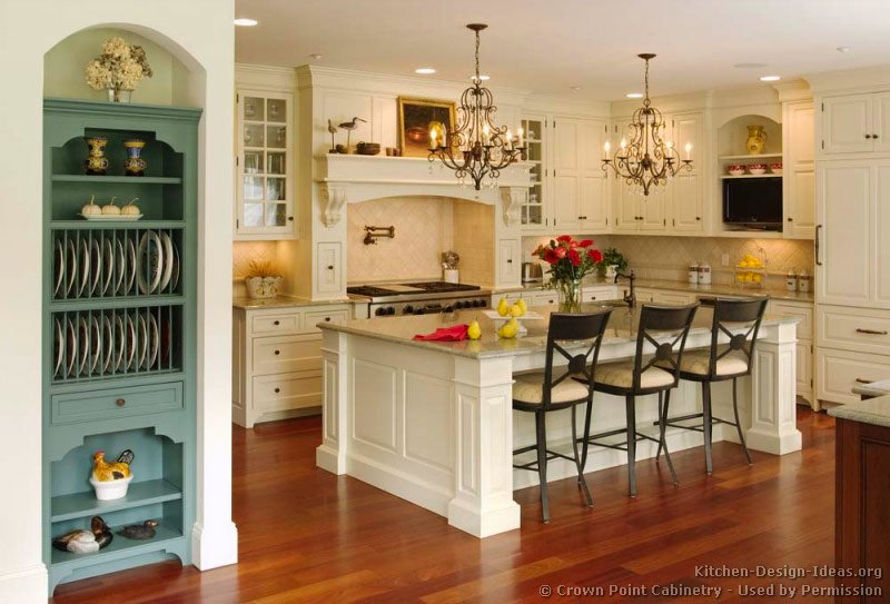 A Victorian kitchen with creamy white cabinets, a mantel wood hood, and a large island with chandeliers above